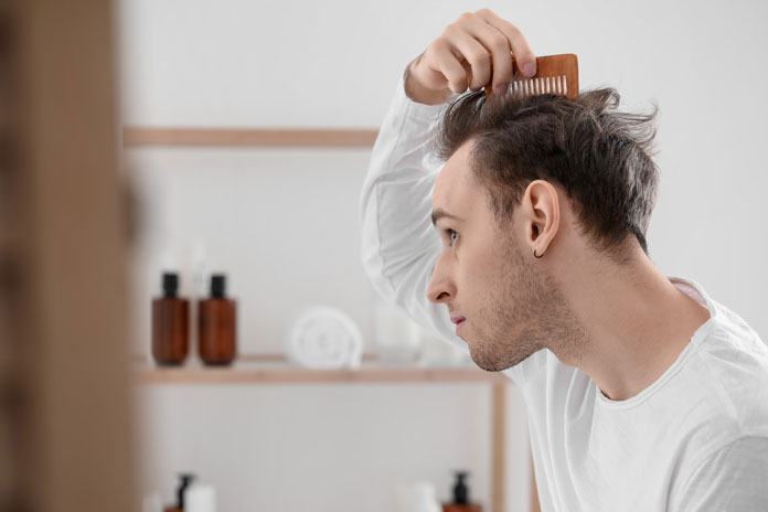 Körperpflege - Junger Mann kämmt sich vor dem Spiegel durch seine Haare