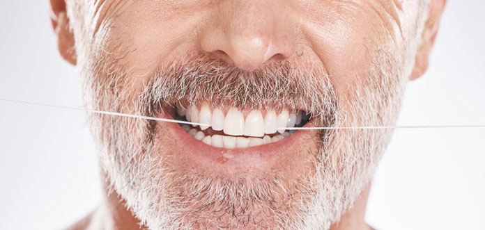 Körperpflege - älterer Mann mit gepflegten Zähnen reinigt seine Zahnzwischenräume mit Zahnseide.
