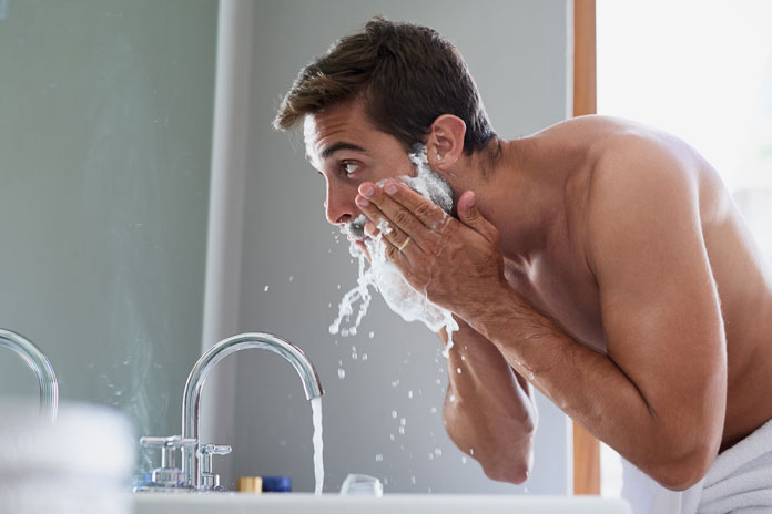 Bartpflege Mann steht morgens im Bad und wäscht sich seinen Bart mit Shampoo und Wasser