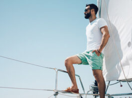 junger bärtiger Mann in Shorts, der auf einer Yacht steht